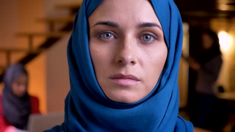 closeup portrait of adult muslim businesswoman in blue hijab looking straight at camera with emotionless facial expression