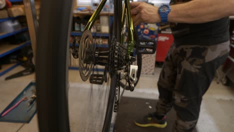 male bicycle mechanic turns crank and adjusts front derailleur whilst on workshop stand