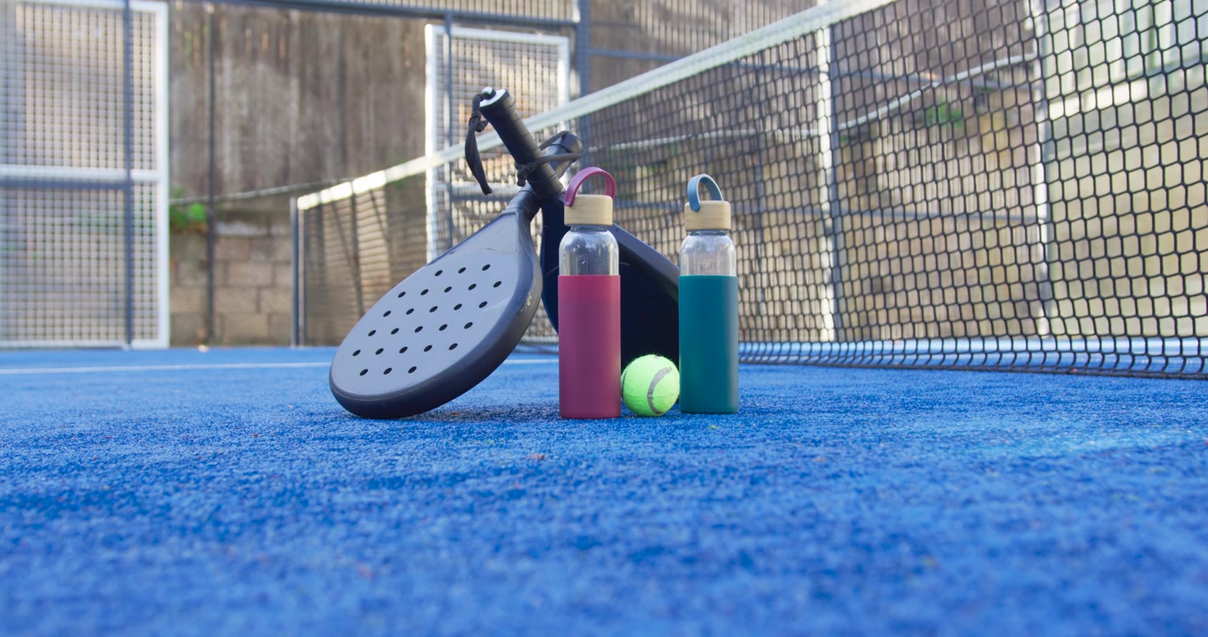 Padelracket og to gjenbrukbare flasker ligger igjen på den blå kunstgressbanen etter at kampen er slutt, med ballen hvilende.