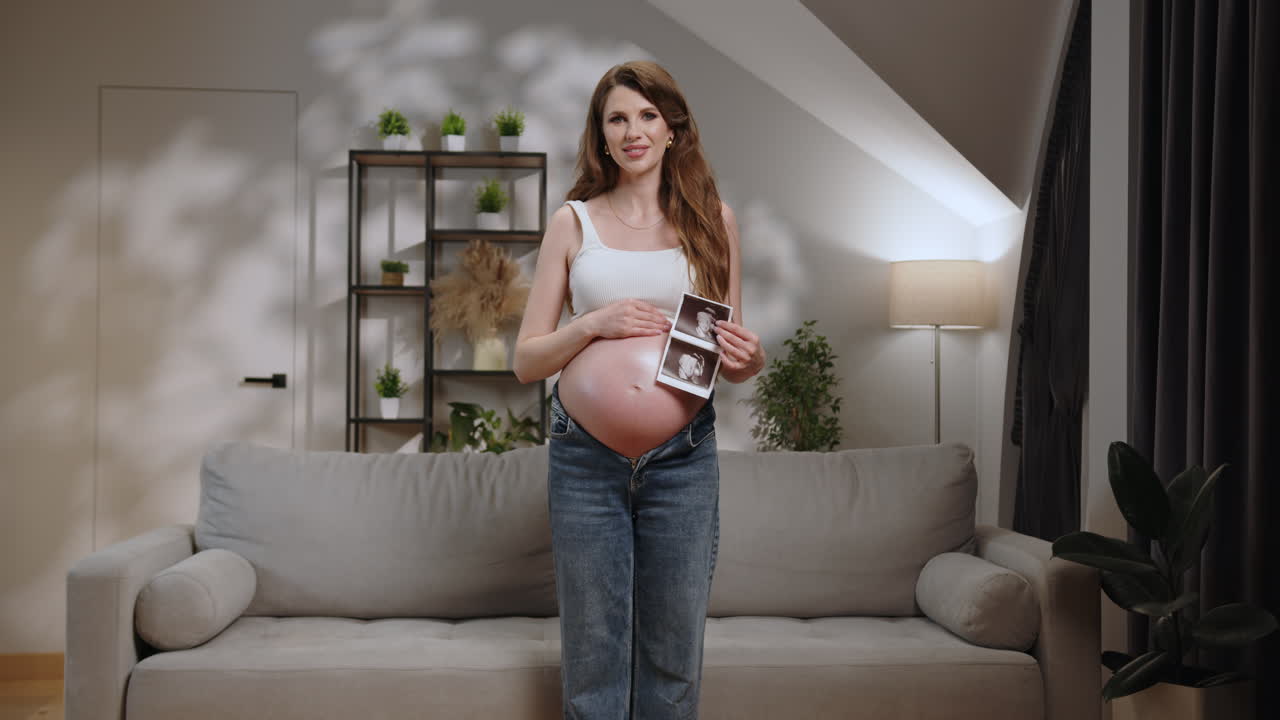 Young expectant mother proudly displays ultrasound images of her unborn baby while standing in a