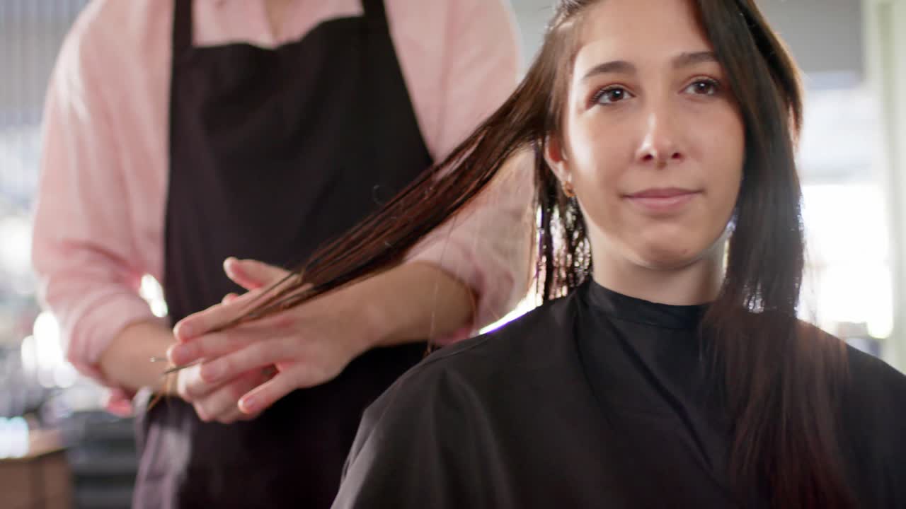 Midsection of caucasian male hairdresser cutting ends of female client's hair at salon, slow motion