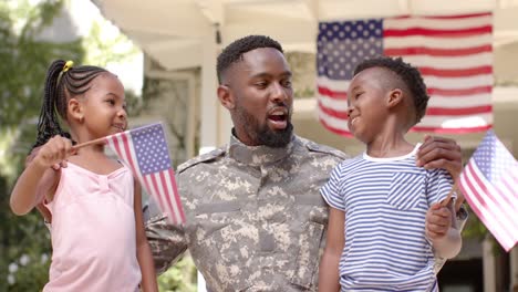 Glücklicher-Afroamerikanischer-Soldat,-Der-Seine-Kinder-Mit-Amerikanischen-Flaggen-Umarmt,-In-Zeitlupe