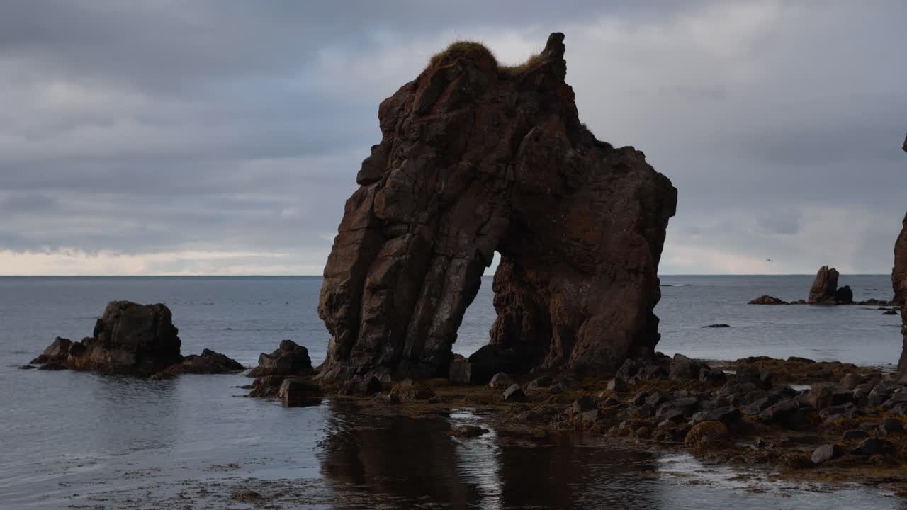 Gatanof sea stock on shore of Iceland island. Seascape during cloudy day. Aerial orbit shot.