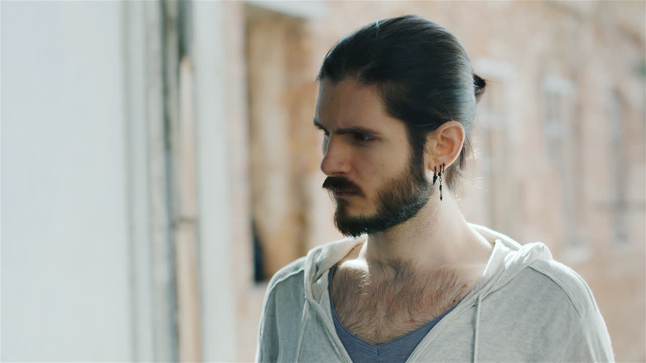 retrato de un pequeño y triste joven barbudo sentado en el alféizar de la ventana en una casa antigua que juega el viento