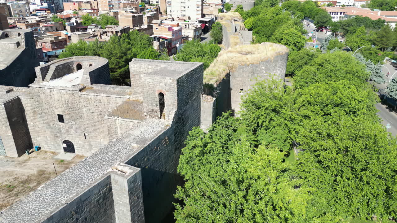 Veduta aerea da drone di antiche mura e torri di fortezza in pietra che dominano una città, mettendo in mostra l'architettura storica in Mesopotamia.