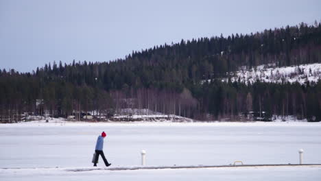 a single person walking in the snow with bright bobble hat in vuokatti finland, left to right