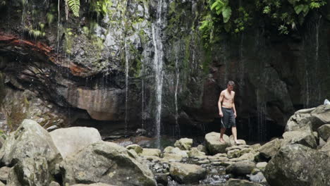 Un-Joven-En-Forma-Caminando-Sobre-Rocas-Lejos-De-Una-Pequeña-Y-Exuberante-Cascada-En-La-Jungla