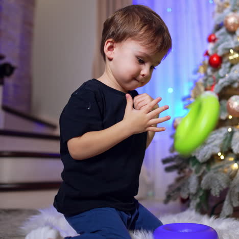 pretty little baby playing with toys at home. kid turns to the cat hiding behind the christmas tree. low angle view.