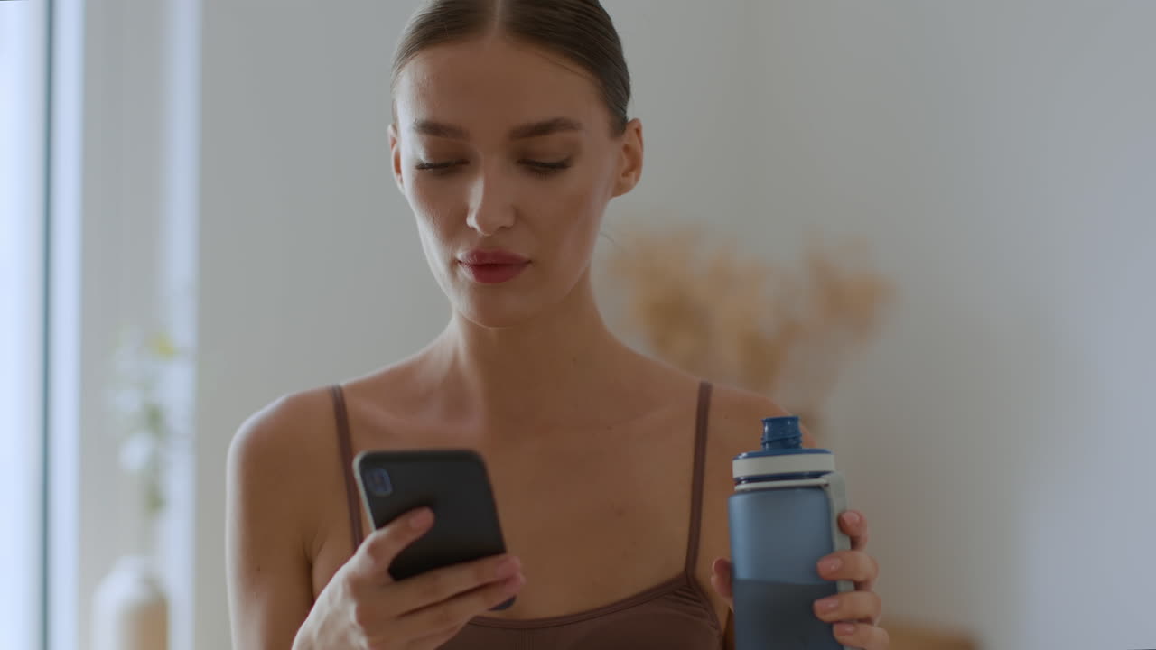 Woman using phone and drinking water at home
