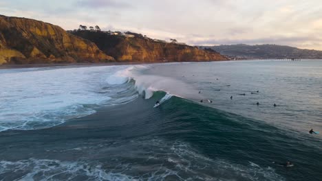 a surfer drops in on a big wave at sunset