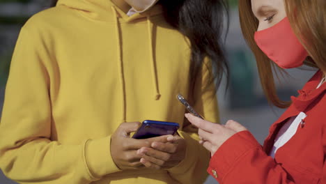 primer plano de amigas multiétnicas que usan teléfonos inteligentes y usan mascarilla