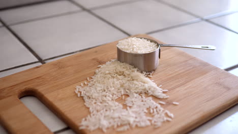 a pile of white rice grains and an ingredients measuring cup on a wooden cutting board in a kitchen slide right