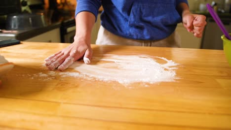 manos esparciendo harina en la encimera de madera preparándose para extender la masa para la masa de pastel