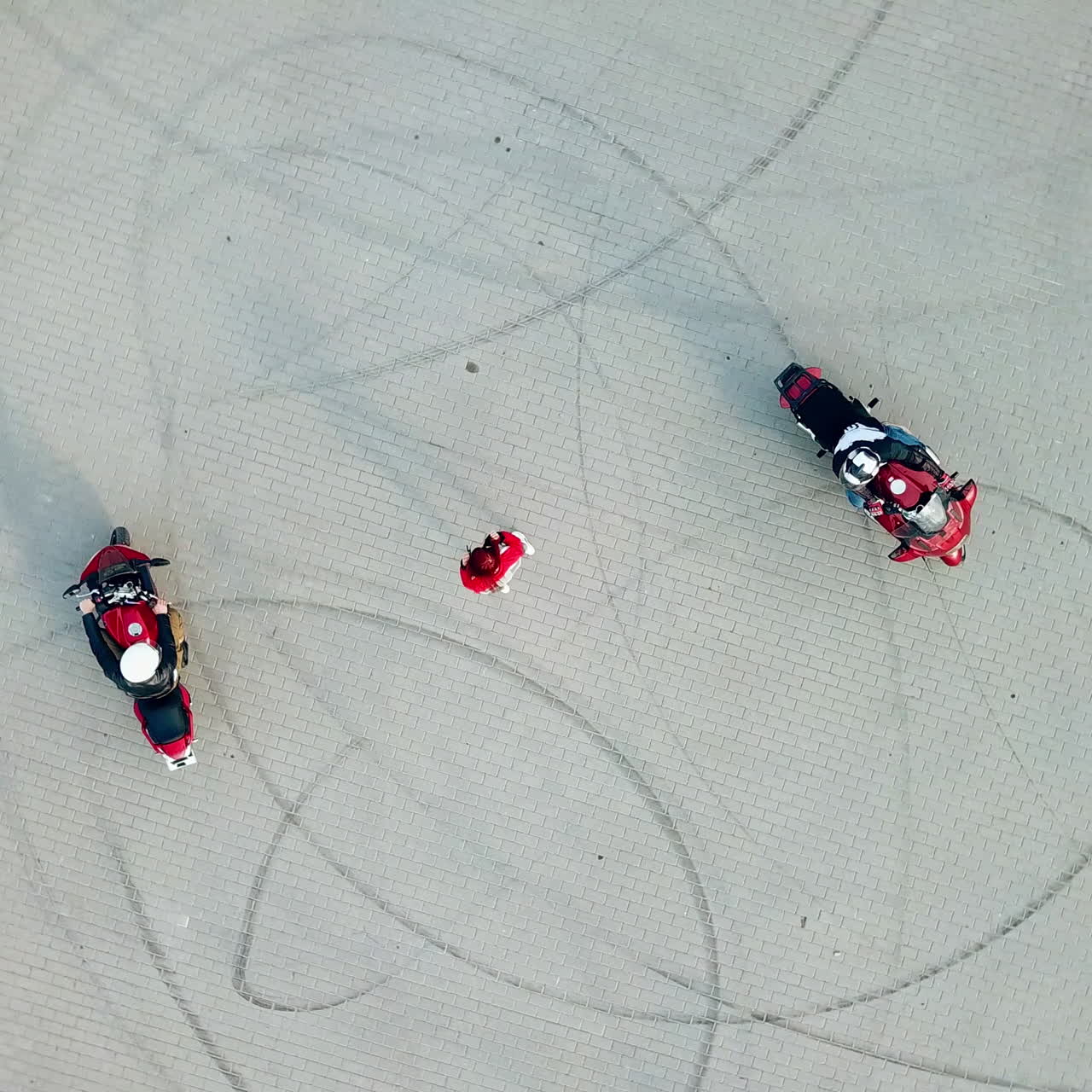 Red-haired woman standing in the centre of two professional motorcyclists riding around her. Top view of a beautiful young female and motorbikers on the road.