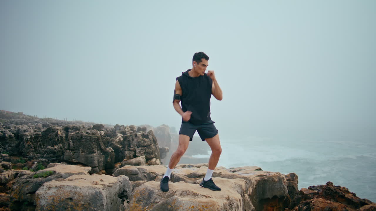 atleta profesional golpea el aire en el acantilado de la costa. fuerte entrenamiento de boxeador en las rocas