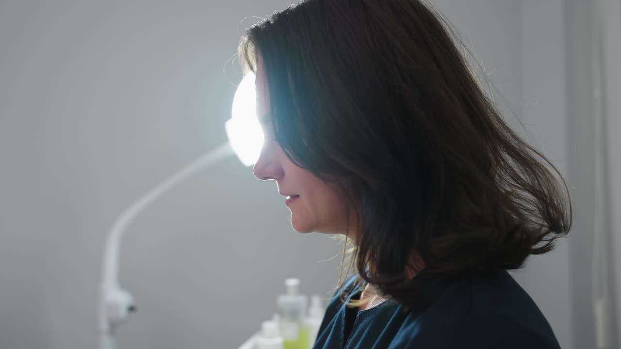 Facialist gently massages client face with wet wipe, client reclining with eyes closed in tranquil state, illuminated by ring light, showcasing soothing skincare treatment in modern spa environment