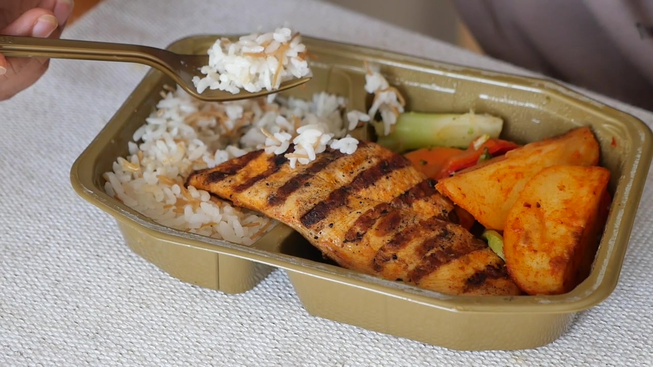 Persona che mangia salmone alla griglia con riso e verdure da un contenitore da asporto