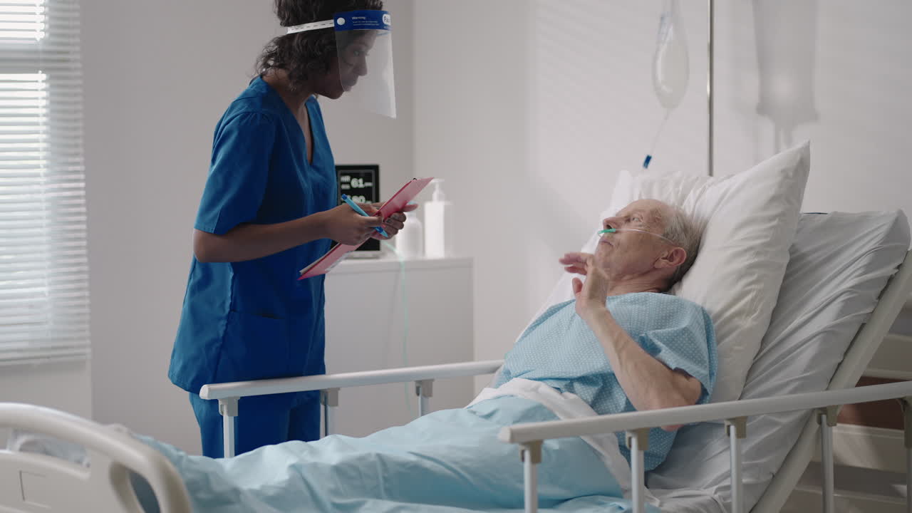 una mujer negra cirujana está hablando con un anciano paciente de sexo masculino acostado en una cama de hospital. una mujer cardióloga especialista en enfermedades infecciosas está hablar con un paciente en la clínica