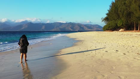 Mädchen-Mit-Rucksack,-Der-Barfuß-Auf-Nassem-Sand-Des-Exotischen-Strandes-Bei-Sonnenaufgang-Mit-Hellblauem-Himmel-über-Dem-Blauen-Azurblauen-Meer-Wäscht,-Das-Ufer-Der-Tropischen-Insel-In-Bali-Geht