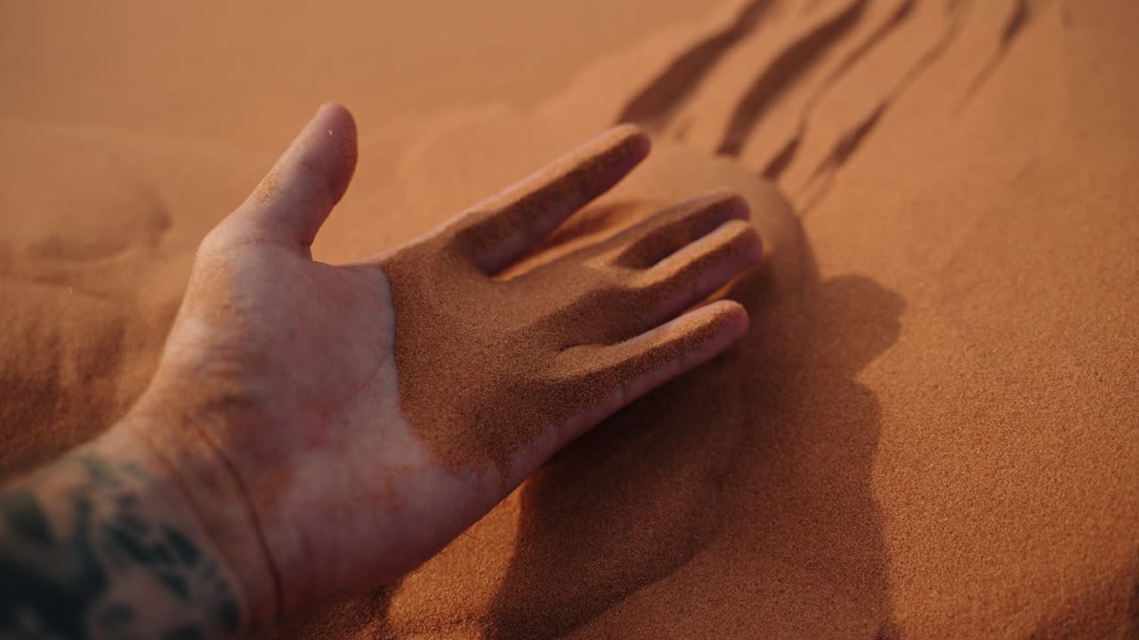 Close-up of a hand holding fine orange sand in the dunes of Merzouga, Sahara Desert, Morocco