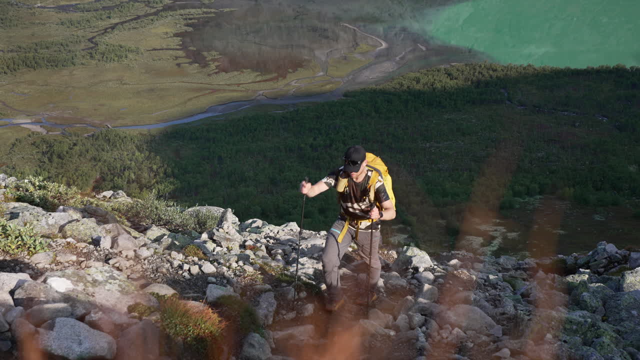 vista de arriba hacia abajo del lado de la colina de senderismo masculino con lago verde y bosques en el fondo, a principios de una soleada mañana de otoño