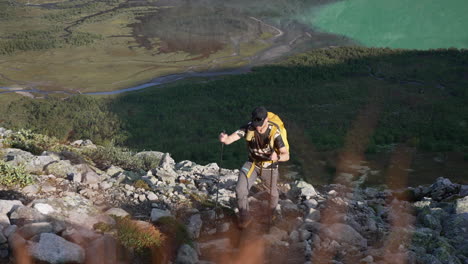 Close-top-down-view-of-male-hiking-hill-side-with-green-lake-and-woods-in-backgroud,-in-early-sunny-autumn-morning