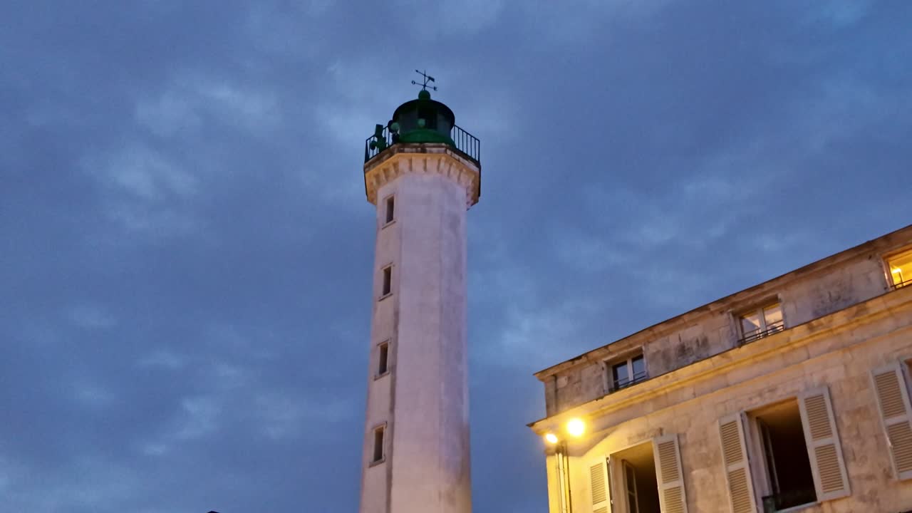 Hải đăng Quai Valin bên cạnh tòa nhà lịch sử dưới bầu trời chạng vạng, La Rochelle, Charente-Maritime, Pháp