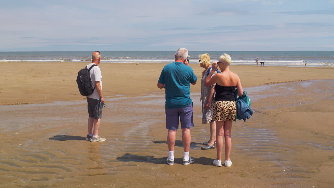 A group of friends shares stories and laughs on a calm beach under a clear blue sky, enjoying their peaceful day together
