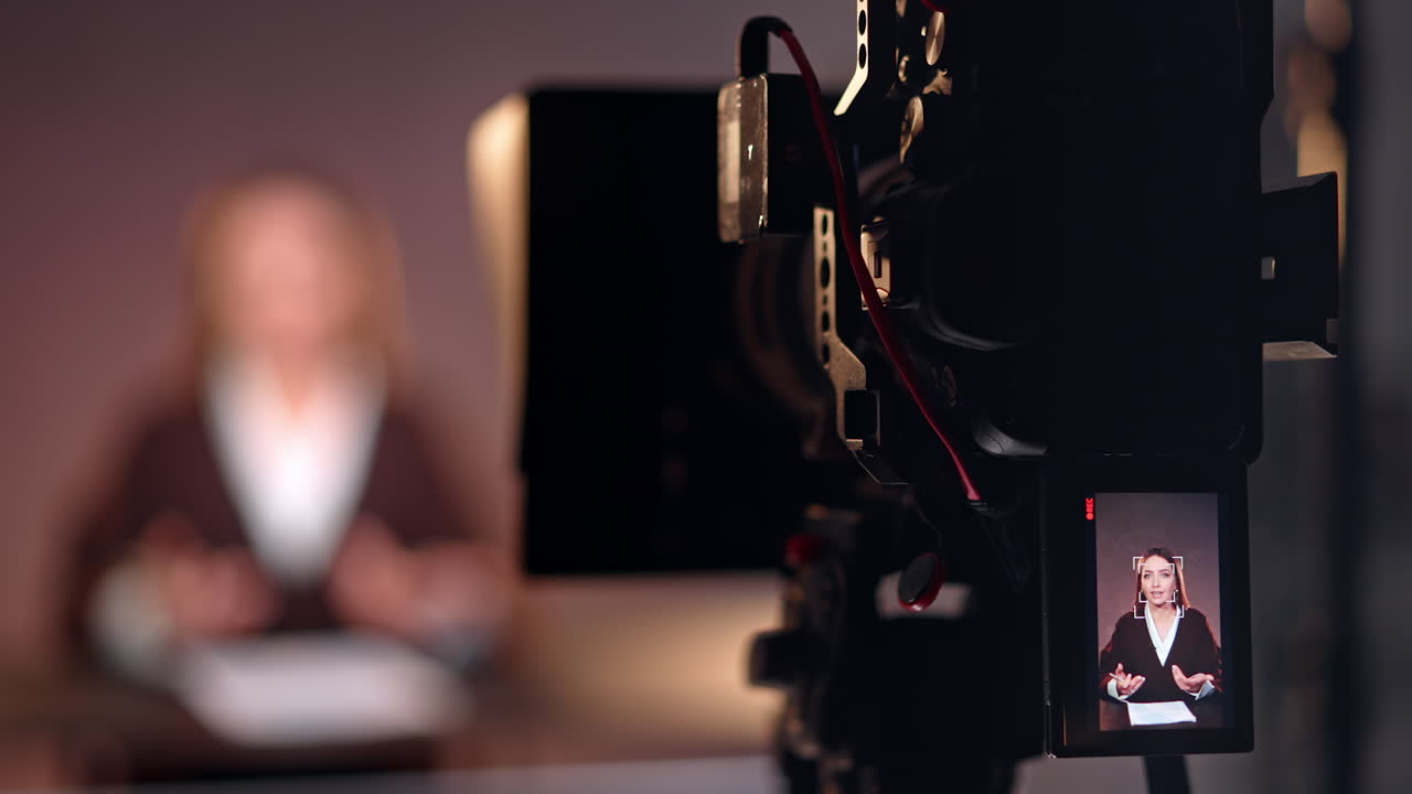Professional camera on tripod filming a female reporter. Studio footage of a program or podcast. Blurred backdrop.