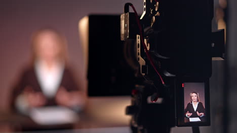 professional camera on tripod filming a female reporter. studio footage of a program or podcast. blurred backdrop.