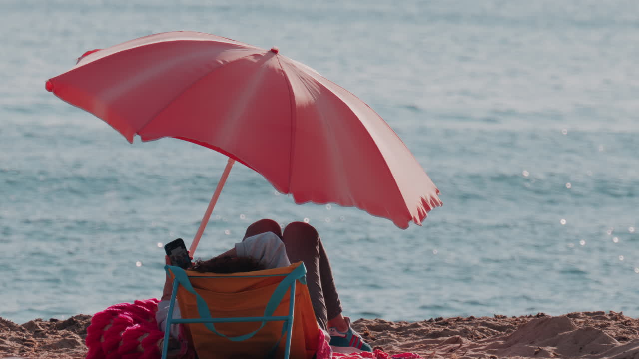 Woman relaxing on the beach, standing on an orange chair and looking at her phone