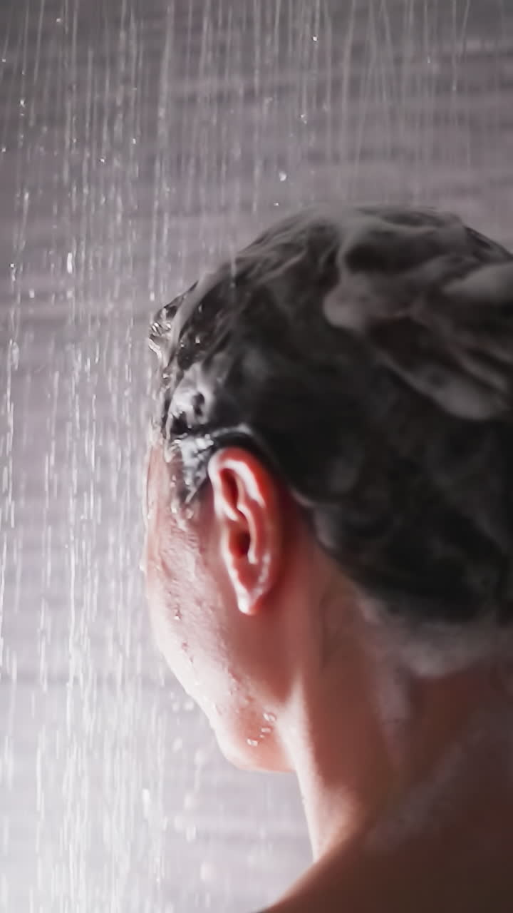 Woman with foamy hair under shower water closeup. Lady washes shampoo from head relaxing in bathroom. Woman takes care of body in modern washroom