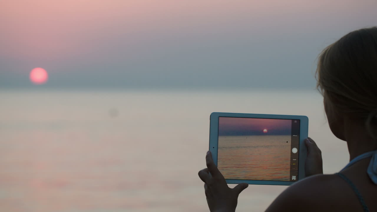 Donna che fotografa il tramonto usando un tablet PC