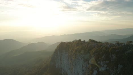 Vista-Aérea-Del-Amanecer-En-Las-Montañas,-Vuela-Por-Encima-De-Los-Escarpados-Acantilados-Hacia-Los-Rayos-Del-Sol