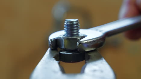 clockwise of a wrench turning a bolt on a screw held by pliers, close up