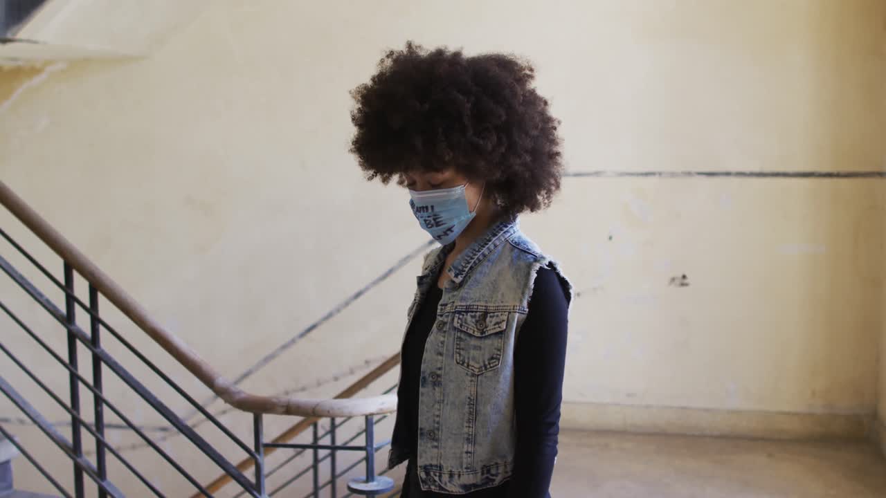 Portrait of african american woman wearing protest face mask standing near the stairs