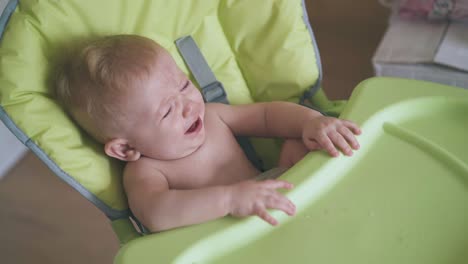 cute boy cries dropping bottle of water in green highchair