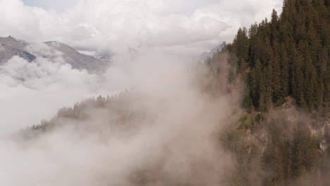 Flying-through-clouds-near-forest-covered-mountain-slope