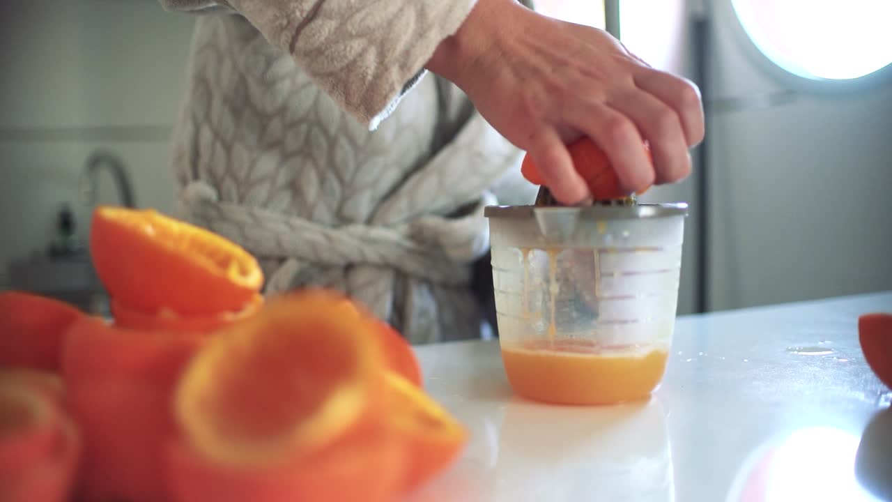 Mujer usando un exprimidor de naranjas, preparando un zumo de naranja en casa.