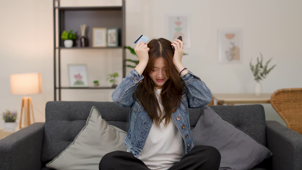 Asian woman on sofa discovers suspicious credit card transaction, grows frustrated in warm living room