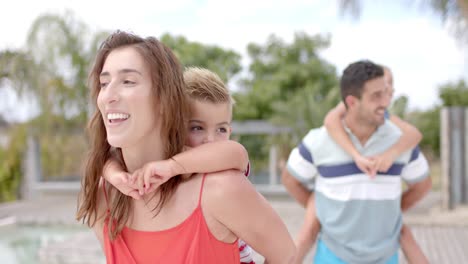 padres caucásicos felices cargando a sus hijos en la piscina de la casa de la playa