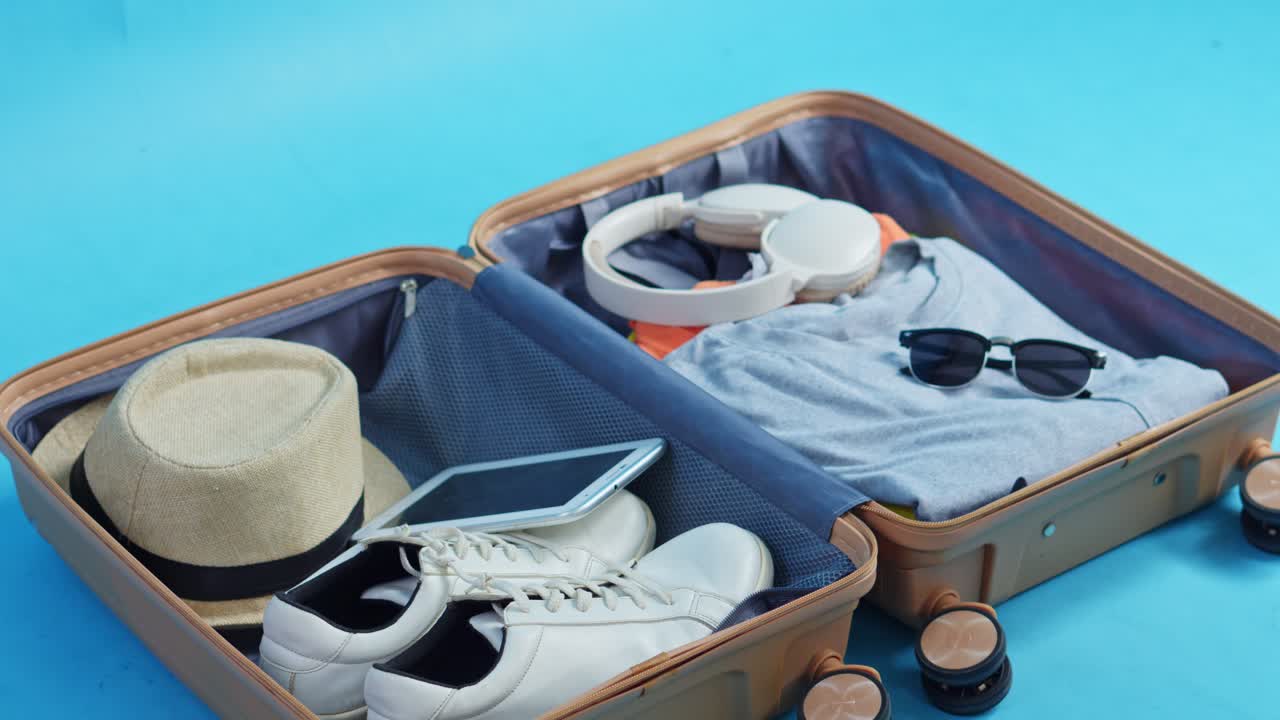 Stop motion de uma mala sendo arrumada com itens essenciais de viagem como roupas, sapatos e tecnologia.