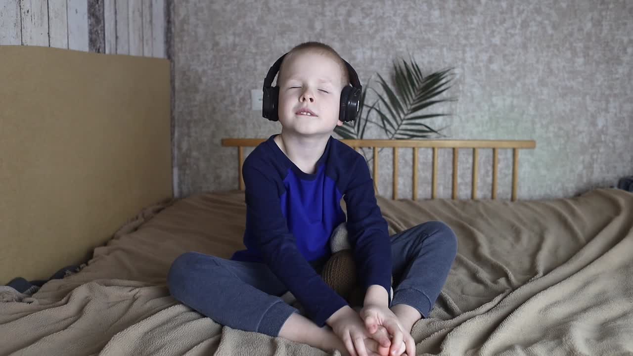 헤드폰을 입은 소년은 잠자리에 들기 전에 어린이들을 위한 명상을 듣습니다. 아이들의 건강한 신경계의 개념. 잠들기 전에 휴식을 취합니다. 금발 소년은 집에서 휴식을 취하고 있습니다. 청각 치료