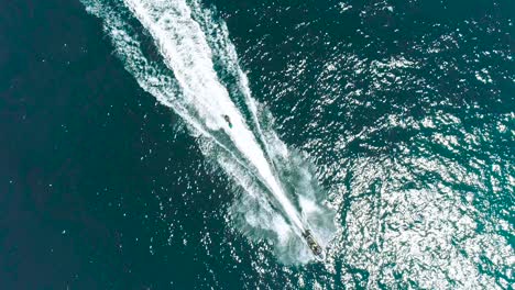 jet ski and surf rider on jet skiing on tropical blue and green sea waterscape. top down aerial footage of sport activity with ocean waves ripple. beautiful high adrenaline and extreme sports scene.