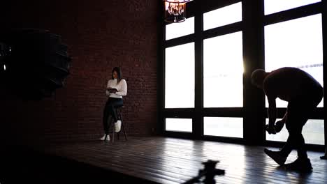sesión de fotos interior con modelo femenino cerca de una ventana brillante y una pared de ladrillo rojo