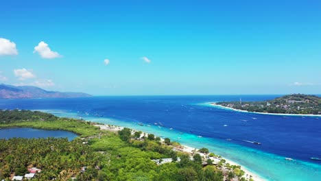 island in indonesia - boats swiftly sailing across the dark blue sea water surrounding the lush island on a sunny day - wide shot