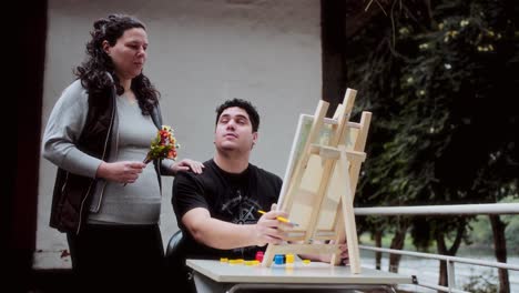 man painting on easel while woman observes