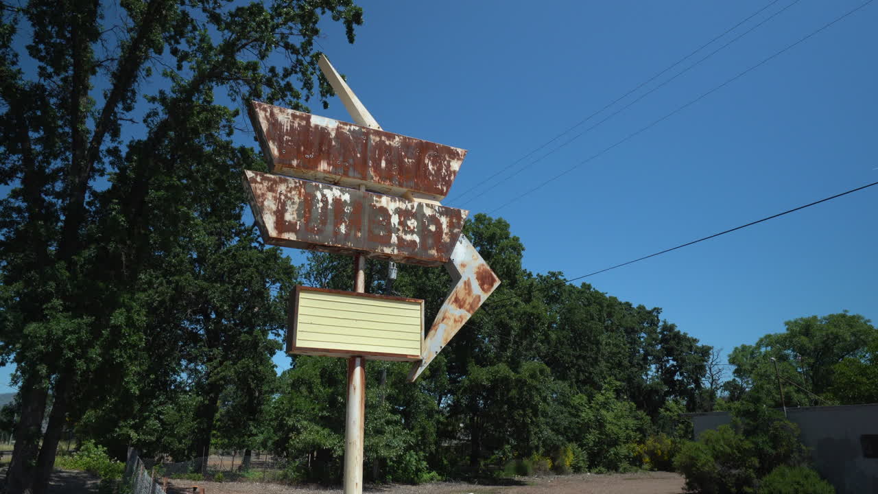 밝고 화창한 날에 버려진 목재 마당 앞에서 녹슨 복고풍 상점 표지판 앞에 철조망이 있는 체인 링크 펜싱