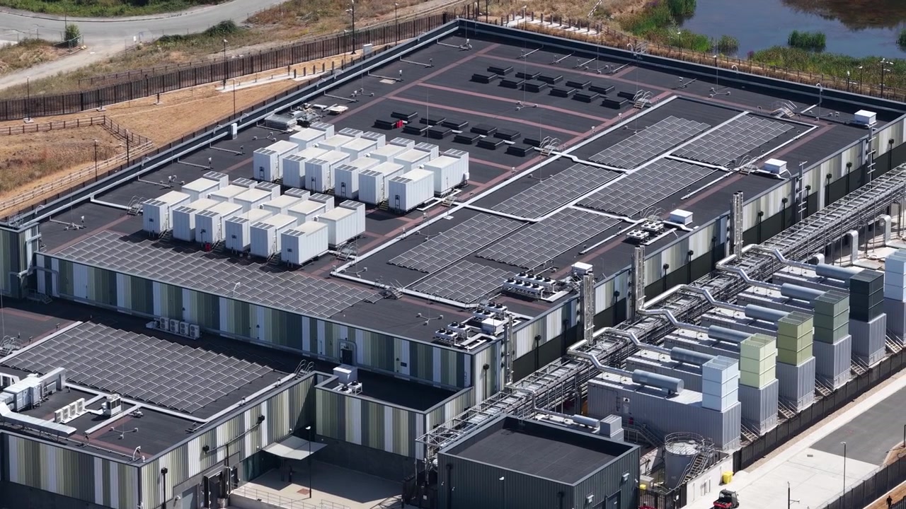Dronebillede fra høj vinkel af et massivt datacenteranlæg med HVAC-køleenheder, transformerstationer og moderne arkitektur, der driver cloud-netværk og AI-systemer