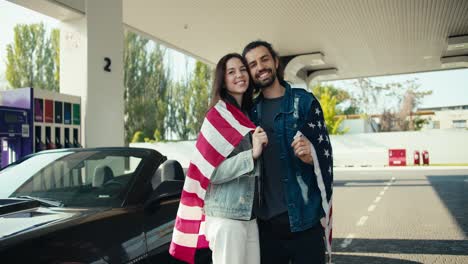 A-young-couple-of-a-guy-and-a-brunette-girl-in-leather-jackets-are-smiling-and-looking-at-the-camera,-they-are-wrapped-in-the-US